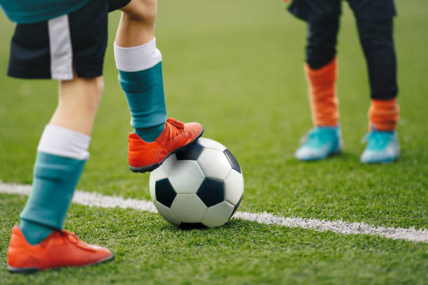 imagen de piernas de futbolista de pie en el banquillo con balón. antecedentes futbolísticos del campo de fútbol y jugadores en un partido. niño con zapatos deportivos pateando pelota - bouncing ball family playing fotografías e imágenes de stock