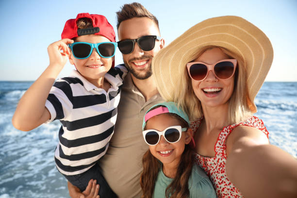 famiglia felice che scatta selfie sulla spiaggia vicino al mare. vacanze estive - family summer portrait nature foto e immagini stock