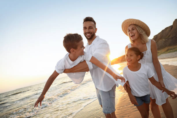 família feliz se divertindo em praia de areia perto do mar ao pôr do sol - clothing love smiling parent - fotografias e filmes do acervo