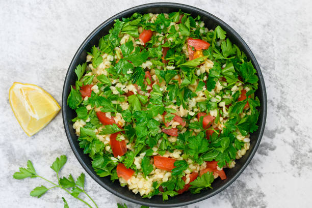 Tabbouleh salad with bulgur, parsley, spring onion and tomato in bowl on grey background. Top view stock photo
