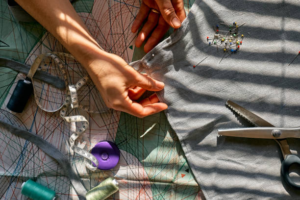 la donna disegna il modello su un tessuto di lino sarta imbastire e cucire in un piccolo studio abiti sartoriali studio di moda, sartoria, concetto di abbigliamento fatto a mano moda lenta consumo consapevole - sewing women tailor textile foto e immagini stock