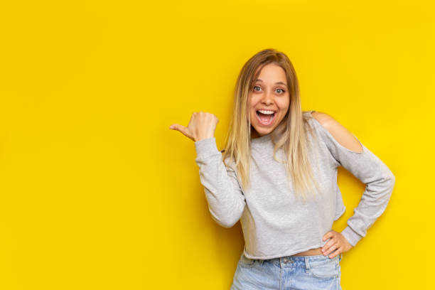 istock A young blonde woman indicates copy empty blank space with her finger on a color yellow background 1361307932