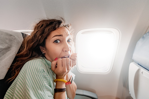 Woman with aerophobia is afraid to fly on an airplane and experiences a panic attack. Emotions of fear and anxiety on the passengers face