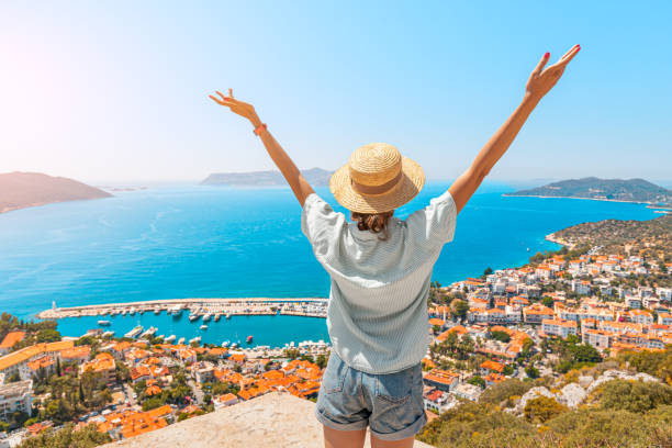 happy woman with open arms stands on the viewpoint and enjoys the panorama of kas resort town of the mediterranean sea in turkey - província de antália imagens e fotografias de stock