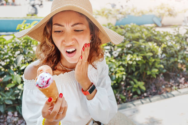 Traveler woman took a bite of cold and sweet ice cream and felt a sharp pain in her teeth due to their hypersensitivity. Medical insurance on vacation concept. Traveler woman took a bite of cold and sweet ice cream and felt a sharp pain in her teeth due to their hypersensitivity. Medical insurance on vacation concept. toothache stock pictures, royalty-free photos & images