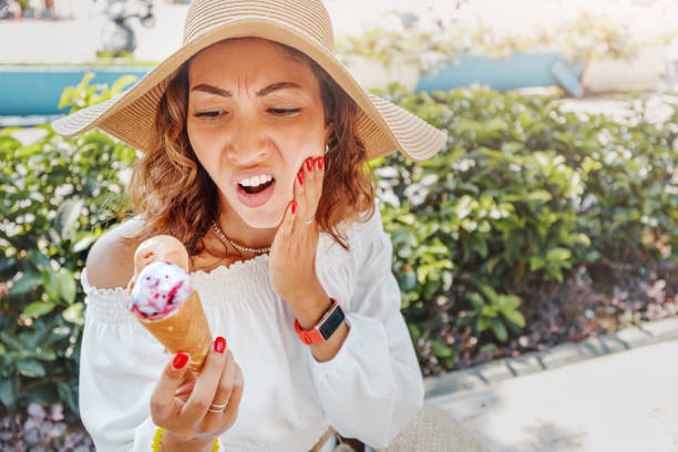 traveler woman took a bite of cold and sweet ice cream and felt a sharp pain in her teeth due to their hypersensitivity. medical insurance on vacation concept. - eating female healthcare and medicine healthy lifestyle imagens e fotografias de stock