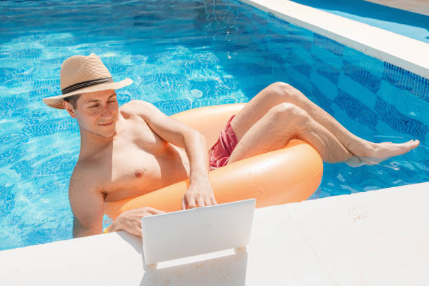 istock Relaxed man floating with inflatable circle in swimming pool and surfing the internet websites at laptop or notebook pc. Leisure weekend and remote freelance work 1361310545