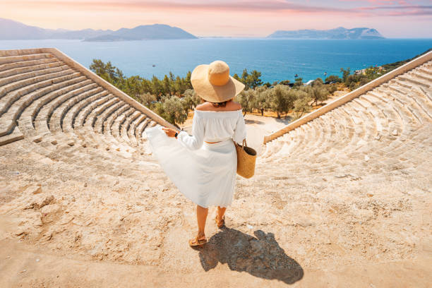 donna affascinante e splendida in abito bianco e cappello esplora l'antico punto di riferimento e le rovine dell'anfiteatro greco o romano sulla costa turistica del mar mediterraneo - rome italy travel traditional culture foto e immagini stock