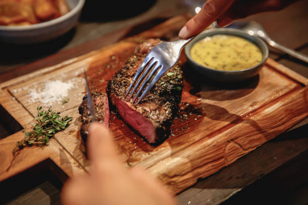 Unrecognizable Woman Eating Steak in High End Restaurant Close up females hands cut a slice of medium rare steak meat. The unrecognizable woman eating dinner in a high end restaurant. steak stock pictures, royalty-free photos & images