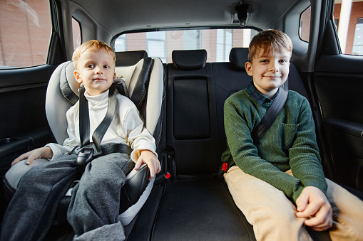 Portrait of two boys sitting in back seat of family car with safety belts and looking at camera