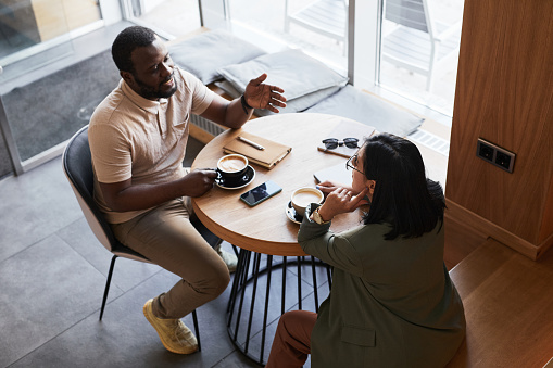 High angle portrait of two young people chatting at table in graphic cafe interior, copy space