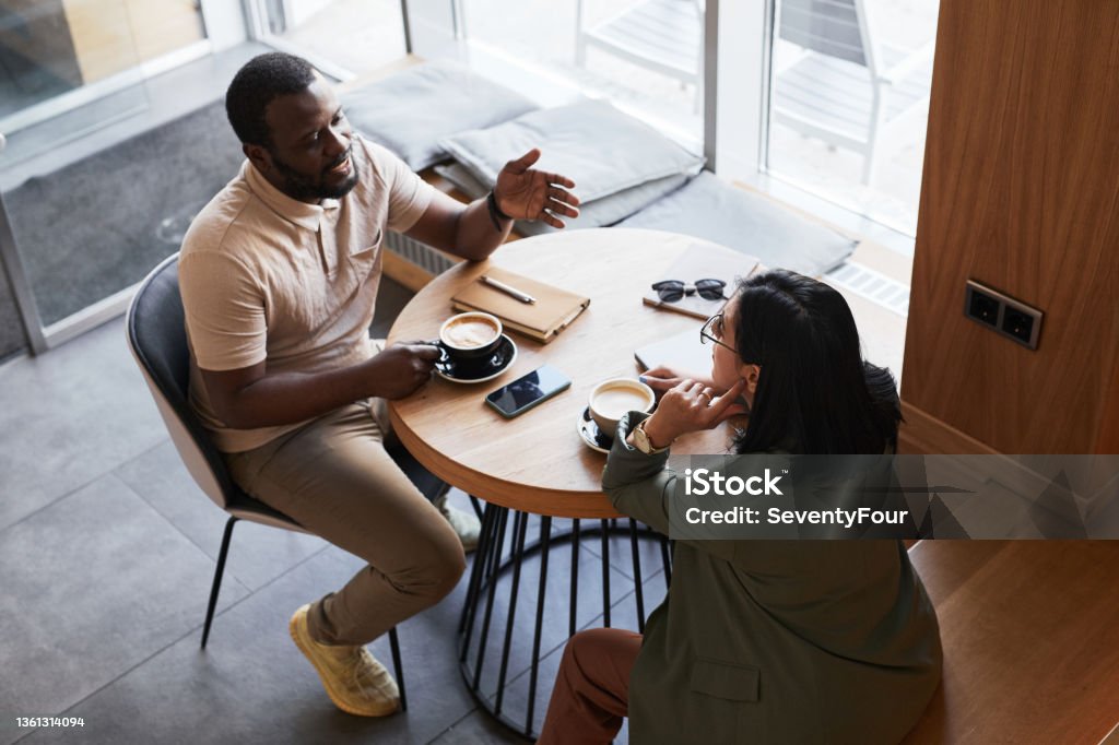 Two Business People in Cafe High Angle High angle portrait of two young people chatting at table in graphic cafe interior, copy space Discussion Stock Photo