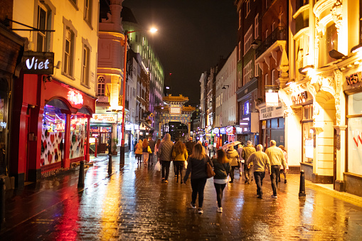 People walking down wet pedestrian street towards Chinese gate, illuminated Chinese restaurants on both sides, Gerrard Street in Soho - London at night