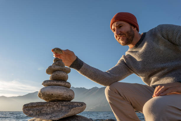 Close up on man's hand stacking rocks by the lake on a sunny day