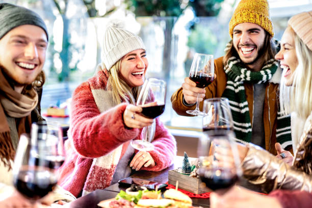 young friends toasting red wine at restaurant patio - happy people having fun together at winery bar wearing winter clothes - dinning life style concept on bright filter with focus on left woman - apres ski fotos imagens e fotografias de stock