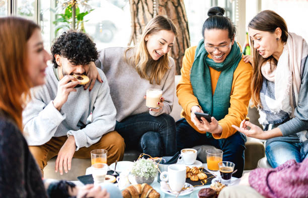 multikulturelle freunde spielen mit handy an der kaffeebar - menschen, die zur brunch-zeit gemeinsam spaß in der cafeteria haben - lifestyle-konzept mit glücklichen männern und frauen im café - heller warmfilter - breakfast eating people teens stock-fotos und bilder