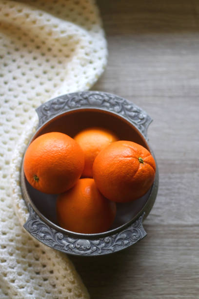 Bowl of Oranges and Blanket Silver bowl filled with fresh oranges and soft knitted blanket on wooden background. Selective focus. antique fruit bowl stock pictures, royalty-free photos & images