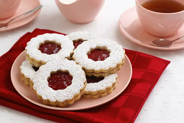 Homemade Linzer Torte cookies with powdered sugar and raspberry jam centers. Teacups and creamer in the background.
