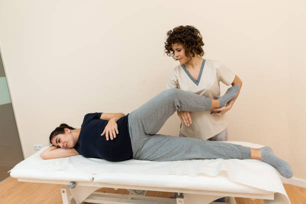 une femme enceinte allongée sur le côté sur une civière pendant qu’un physiothérapeute masse ses jambes dans un centre de santé. - reflexology massaging recovery sport photos et images de collection