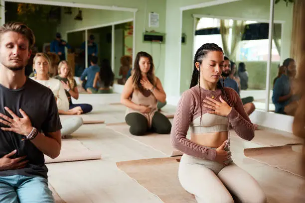 Diverse group of students meditating with their eyes closed and touching their chakras during a yoga class