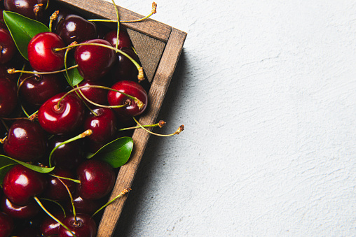 Fresh cherries in a wood container, white background.