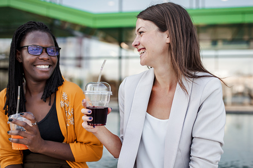 Beautiful black and white business women sitting near the fountain and drinking some fresh juices