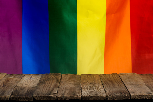 Empty rustic wooden table made from old planks with pride rainbow flag on background.