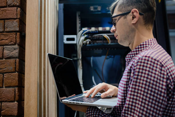 dans la salle des serveurs, un technicien / ingénieur informatique / tient l’ordinateur portable - computer plan fiber optic engineer photos et images de collection