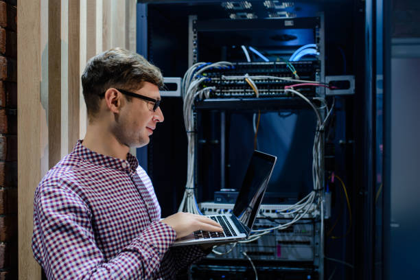 In the server room a technician/ It engineer/ hold the notebook In the server room a technician/ It engineer/ with glasses hold the notebook and adjust the internet  connecting or fix the server error. computer plan fiber optic engineer stock pictures, royalty-free photos & images