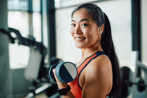 Feliz mujer atlética asiática haciendo ejercicio con pesas de mano en un gimnasio y mirando a la cámara. photo