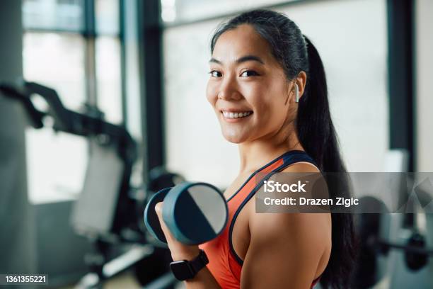 Happy Asian Athletic Woman Exercising With Hand Weights In A Gym And Looking At Camera Stock Photo - Download Image Now