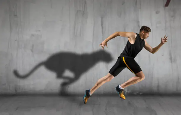 Sporty young man running on urban background. Sports banner with cheetah shadow on the wall.