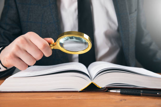 istock a man examines a book with a magnifying glass 1361355373