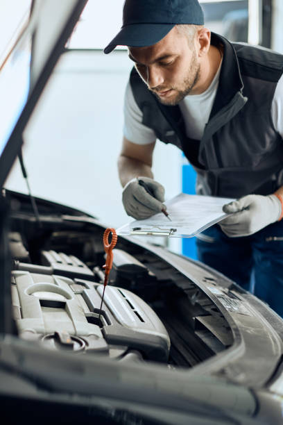 istock Auto repairman writing data while examining car oil in a workshop. 1361355533