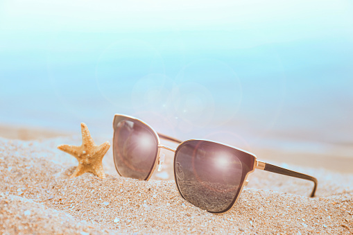 Stylish sunglasses and starfish on sandy beach