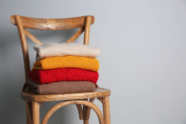 istock Stack of folded knitted sweaters on wooden chair. Space for text 1361356986