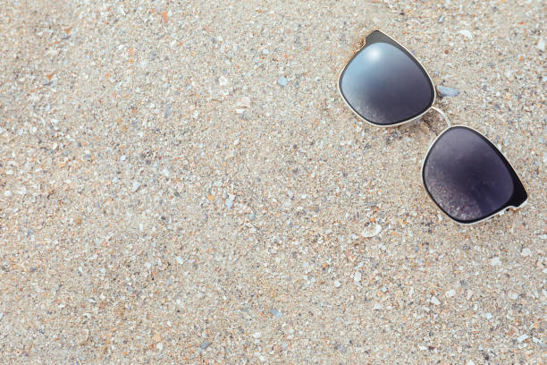 Stylish sunglasses on sandy beach, top view. Space for text