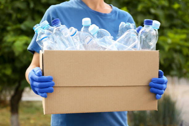 istock Woman holding cardboard box with used plastic bottles outdoors, closeup. Recycling problem 1361358181