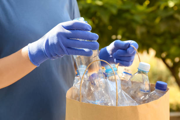 istock Woman putting used plastic bottle into paper bag outdoors, closeup. Recycling problem 1361358447