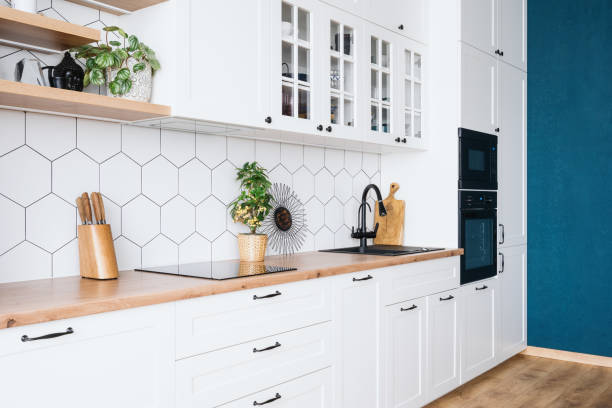 Contemporary kitchen interior design with white wood furniture Side view of modern kitchen interior design with blue wall. White wood furniture, appliances and decor. Spacious apartment after renovation. Bright real estate for sale cupboard stock pictures, royalty-free photos & images