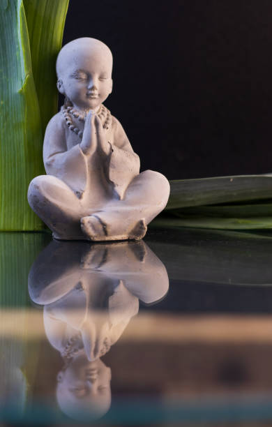 istock Meditating Buddha figure on black background and green leaves 1361365187