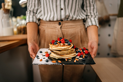 Close-up of hands of woman holding plate of pancakes with berries and powdered sugar
