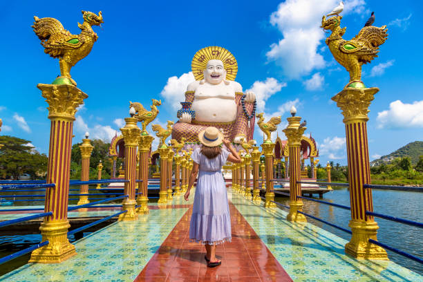 Woman at Giant happy buddha Samui Woman traveler wearing blue dress and straw hat at Giant smiling or happy buddha statue in Wat Plai Laem Temple, Samui, Thailand ko samui stock pictures, royalty-free photos & images