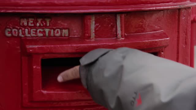 Hand of a Young Man sending Mail, Posting a Letter Into a Post Box, UK. Close Up. 4K Resolution.