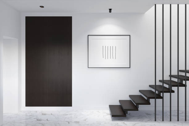 hall d’entrée minimaliste avec affiche horizontale illuminée sur un mur blanc, armoire en bois sombre près de la porte d’entrée, escaliers avec marches en bois sombre, sol en marbre, plafond avec lampes intégrées. - closet hotel door contemporary photos et images de collection