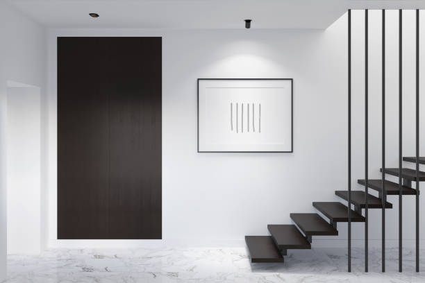 минималистская прихожая с подсвеченным горизонтальным плакатом на белой стене, шкаф из темного дерева возле входной двери, лестница с темн - marble design indoors corridor стоковые фото и изображения