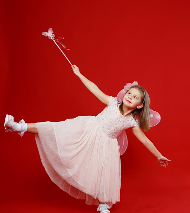 A cute little girl in a fairy costume with wings and a magic wand on a red background.