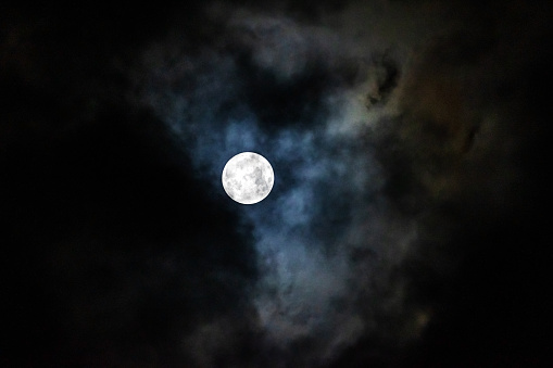 Full moon in the night sky among the clouds. Dramatic sky, bright clouds.