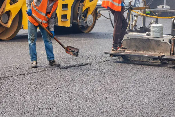 Photo of Road workers pave fresh asphalt using a shovel, paver and vibratory roller.