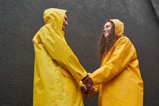Horizontal medium low angle shot of Caucasian man and woman wearing yellow raincoats holding hands looking at each other
